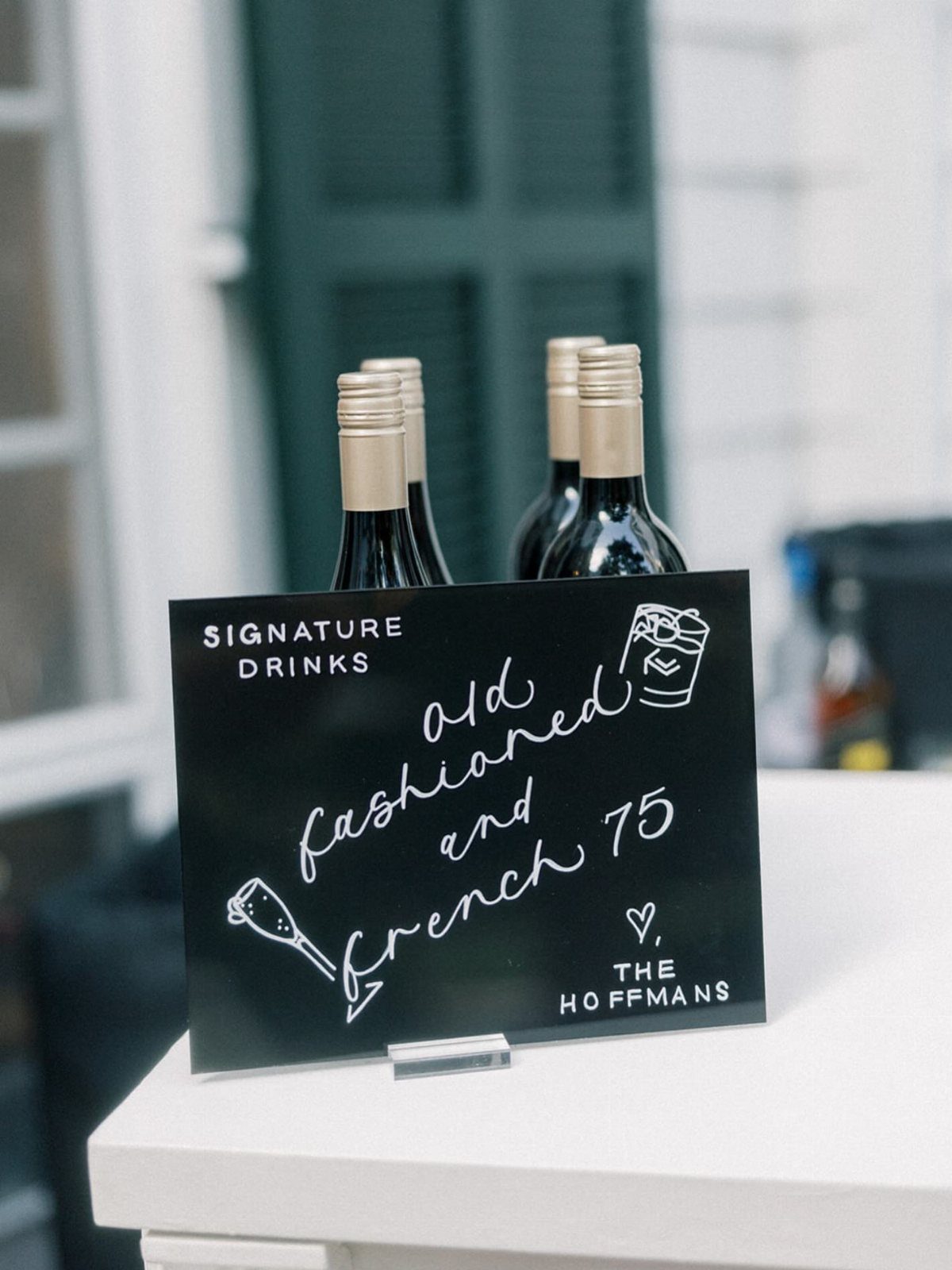 Signature drinks sign listing Old Fashioned and French 75 cocktails with wine bottles.