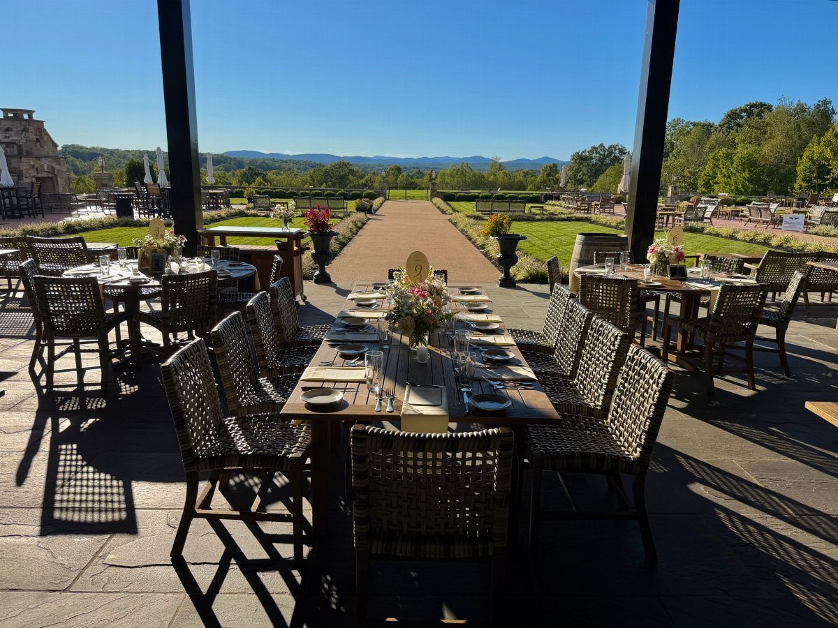 Outdoor patio with set dining tables overlooking a garden path and distant mountains.