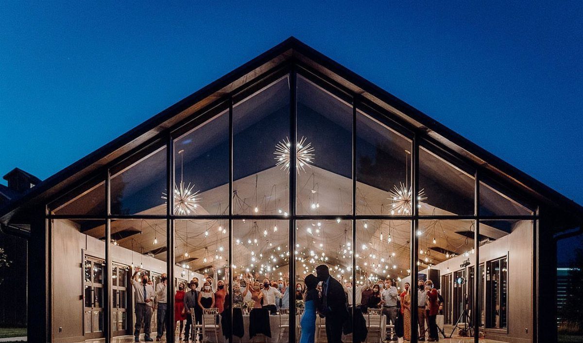 Modern glass pavilion with starburst chandeliers and guests inside during a twilight event.