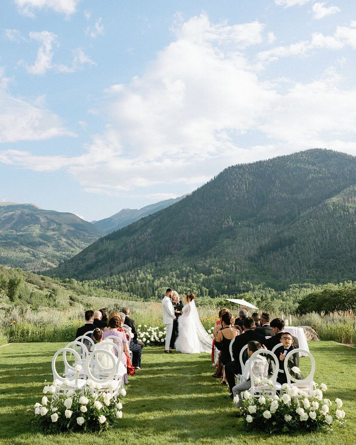 Wedding ceremony on a green lawn with guests and mountains in the background