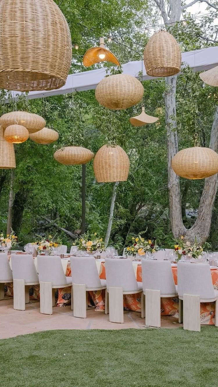 Outdoor dining table with white chairs under hanging woven wicker pendant lamps and trees