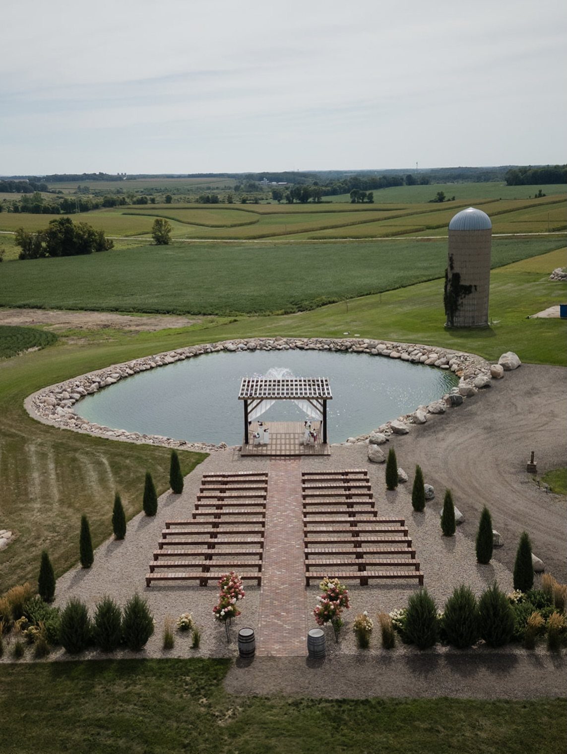 Wooden wedding benches and a white pergola beside a pond in a rural landscape
