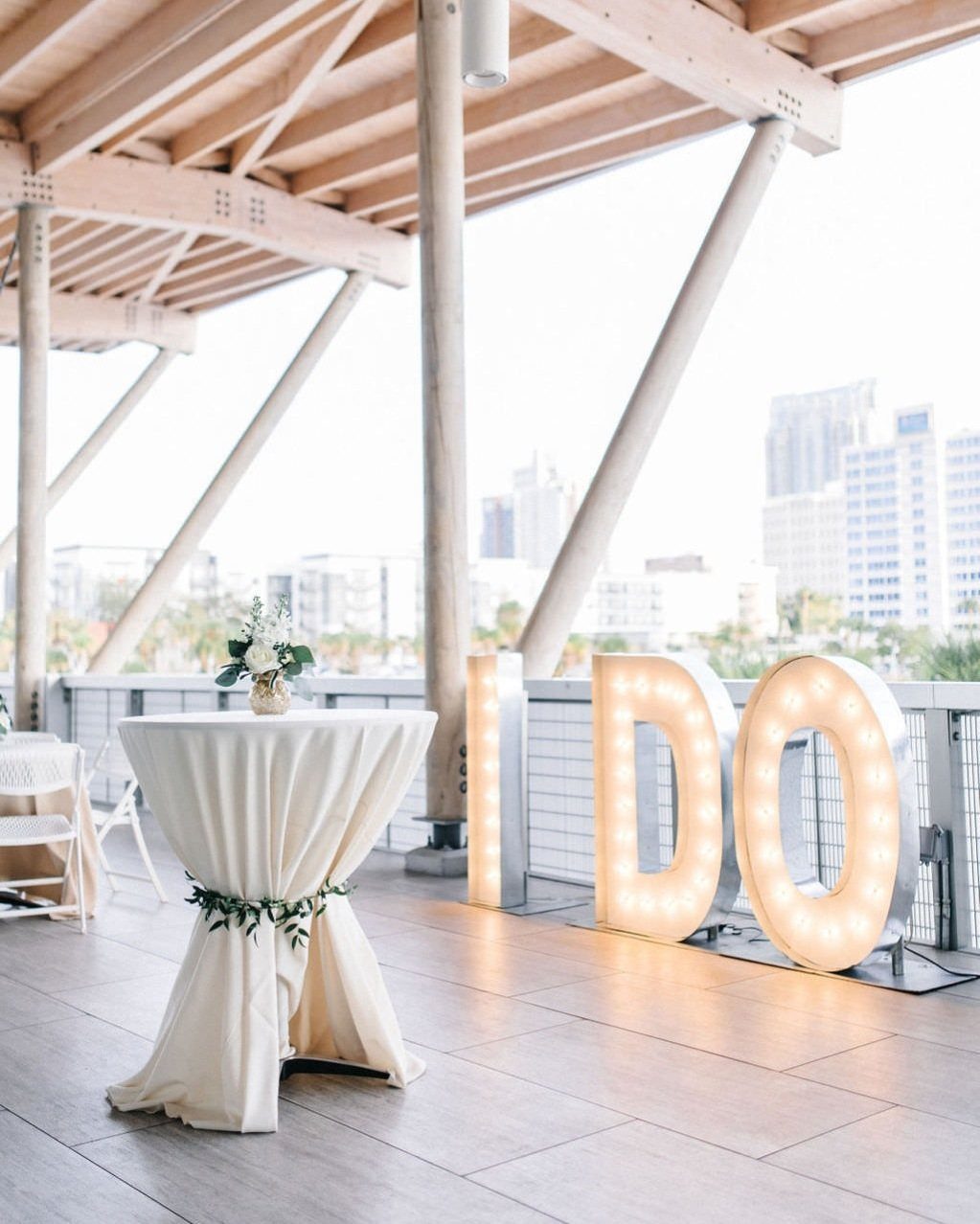 Outdoor wedding patio with a white cocktail table and glowing I DO letters.