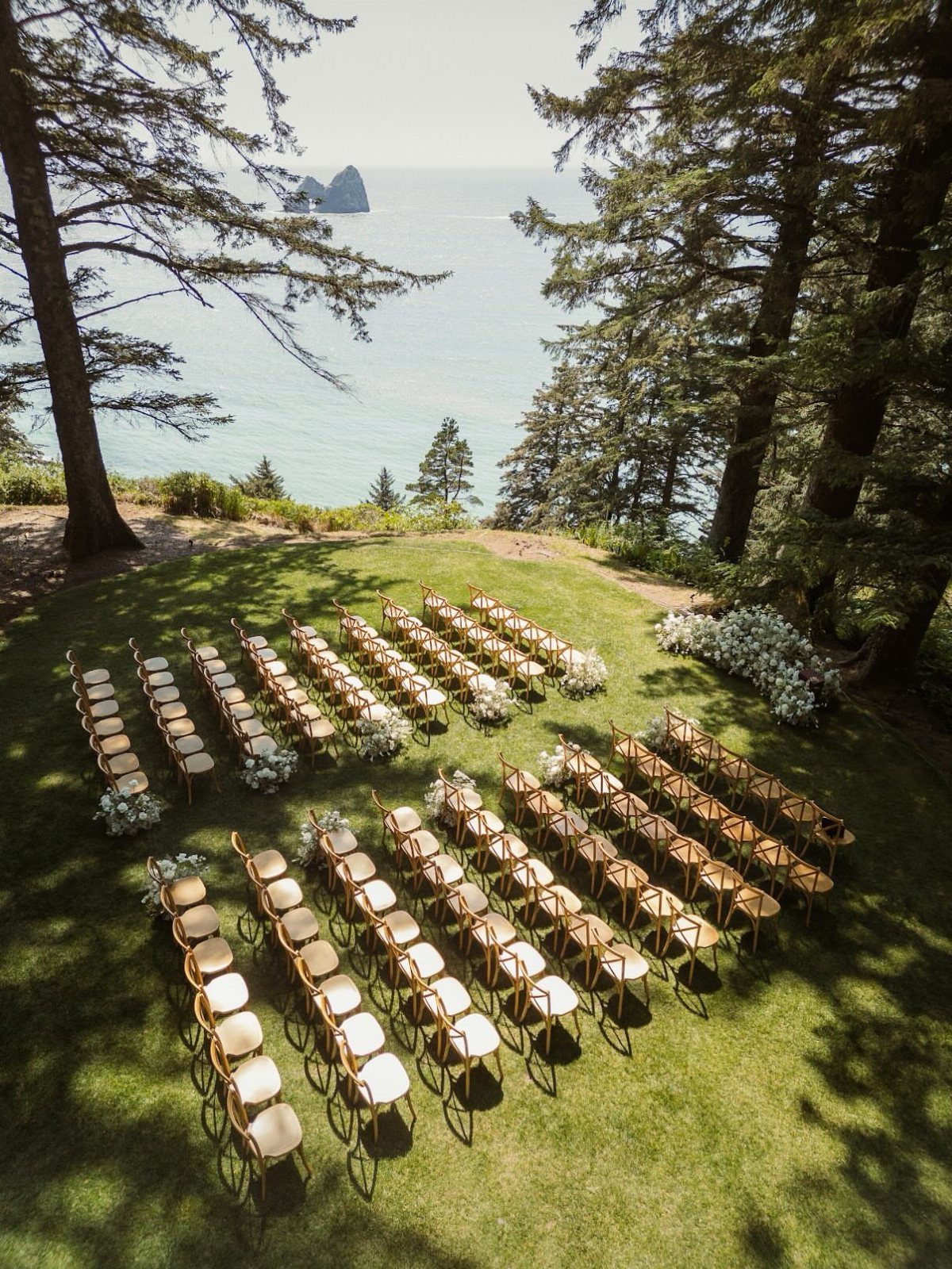 Gold wedding chairs on a grassy cliff overlooking the blue ocean and rocky islands.