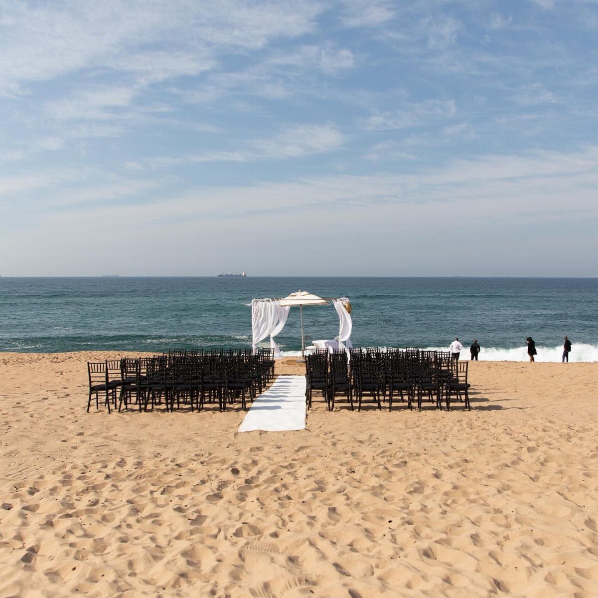 Beach wedding ceremony setup with brown chairs and white altar on sandy shore