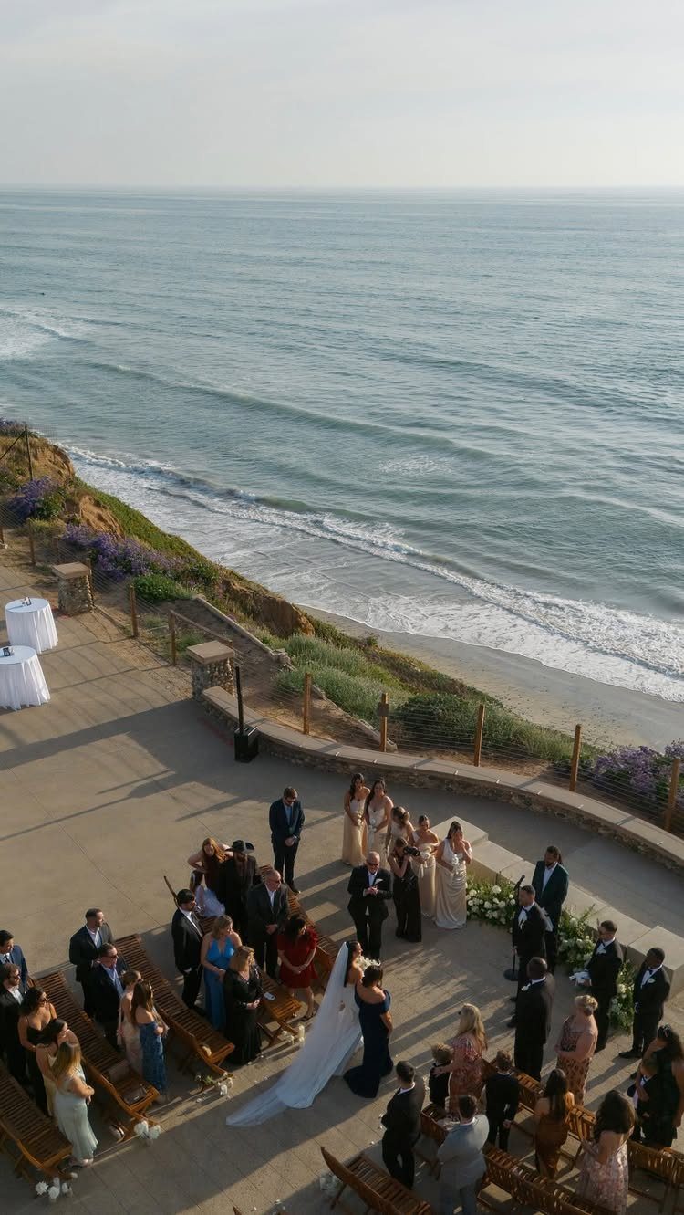 Wedding ceremony on a cliffside terrace overlooking the blue ocean with guests seated.
