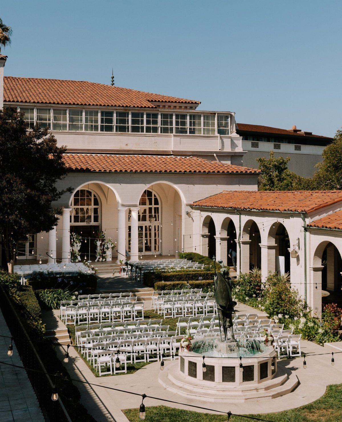 Outdoor wedding ceremony setup with white chairs and a fountain at The Ebell.
