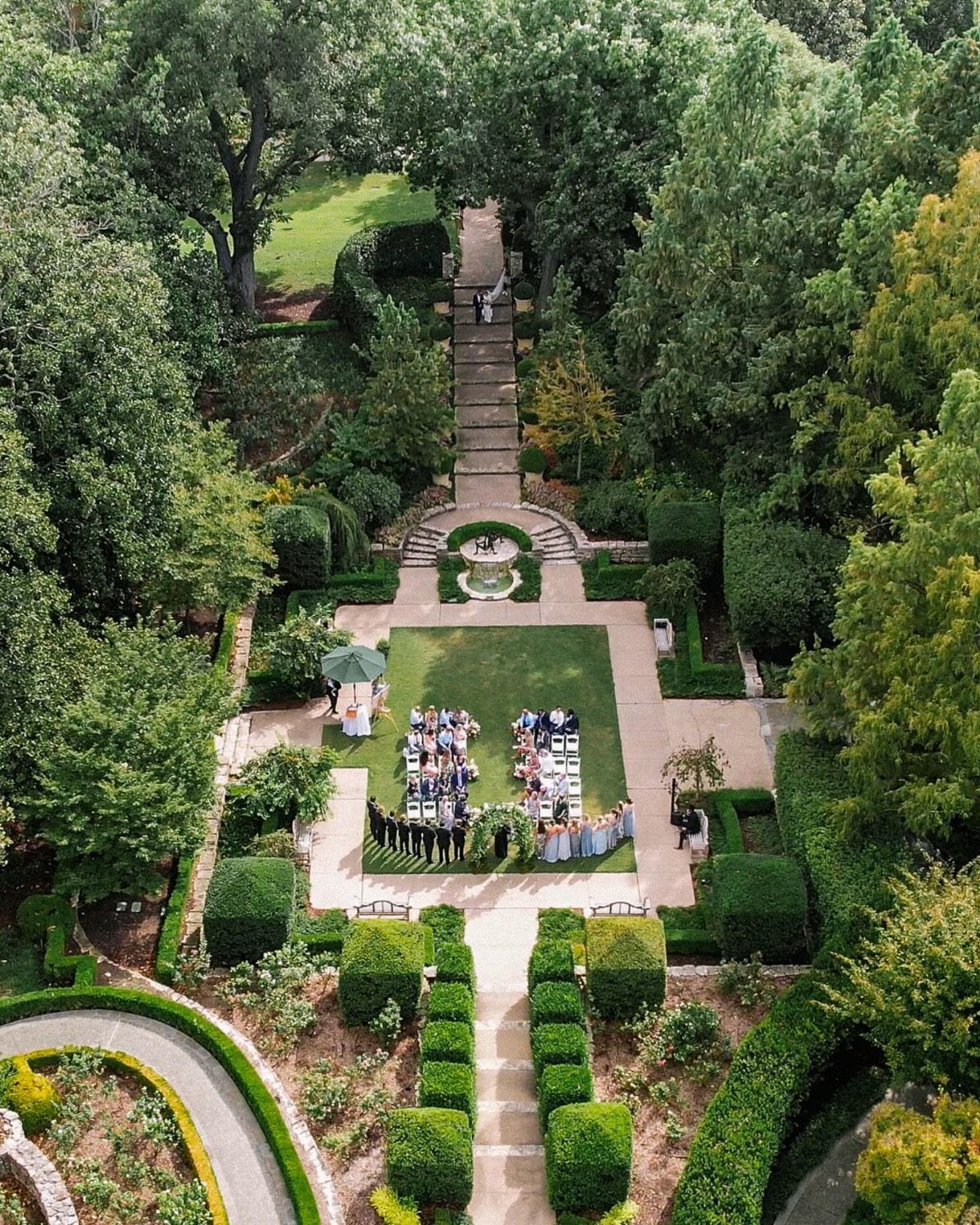 Formal garden wedding ceremony with guests seated on a lawn surrounded by manicured hedges.