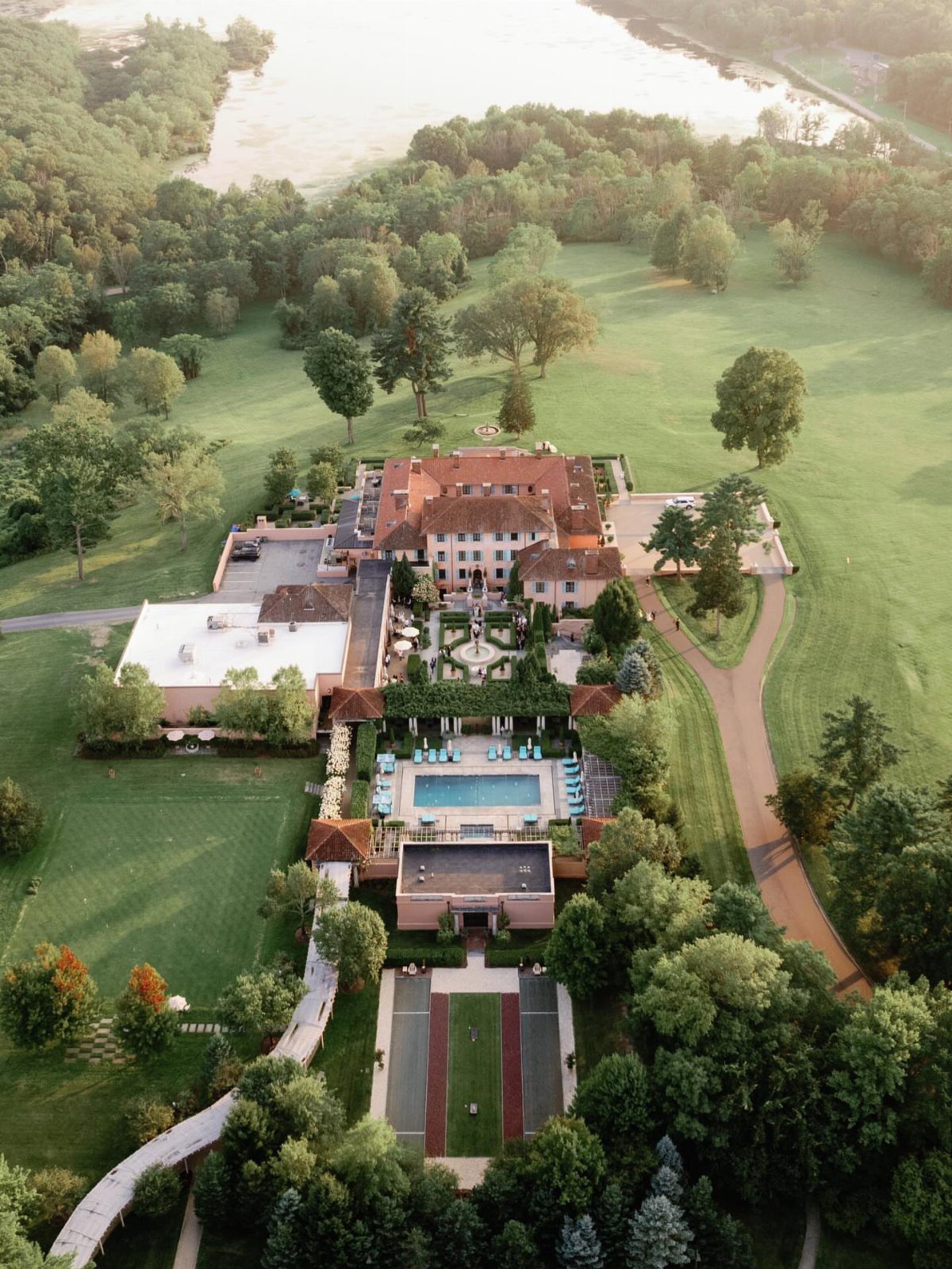 European-style mansion with red roof, swimming pool, and gardens surrounded by lush greenery.