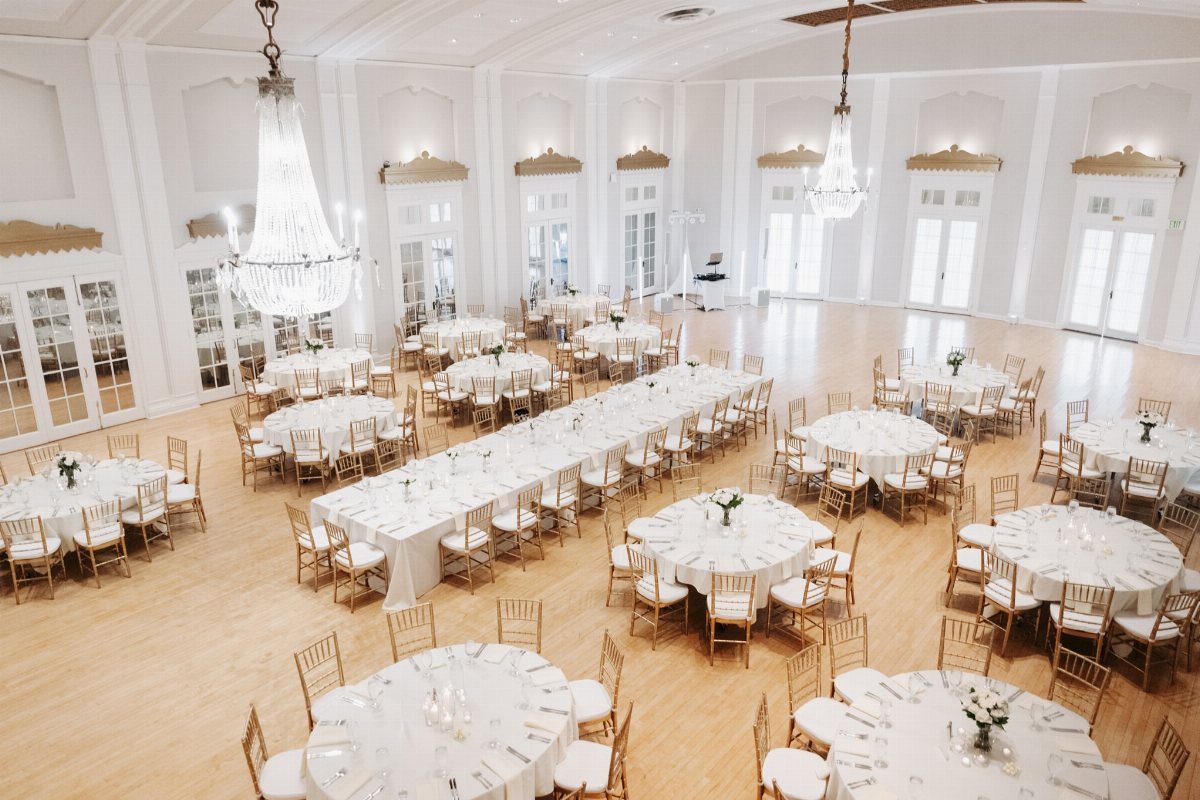 Elegant ballroom with white table linens, gold chairs, and large crystal chandeliers.