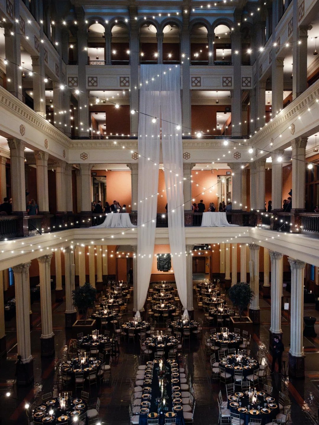 Grand indoor event space with classical columns, fairy lights, and elegant dining tables.