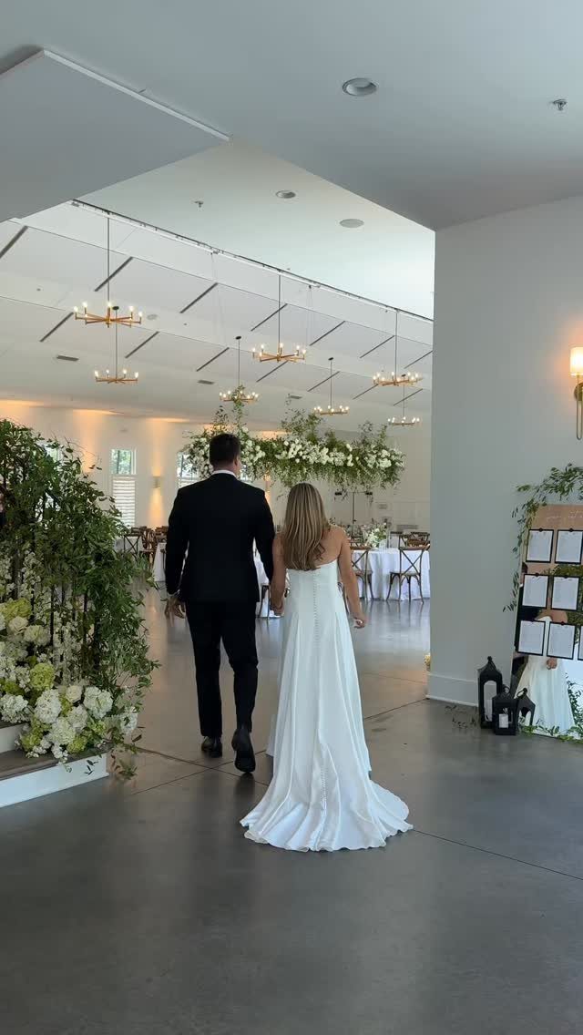 Bride and groom walking into a modern white event space with gold chandeliers.