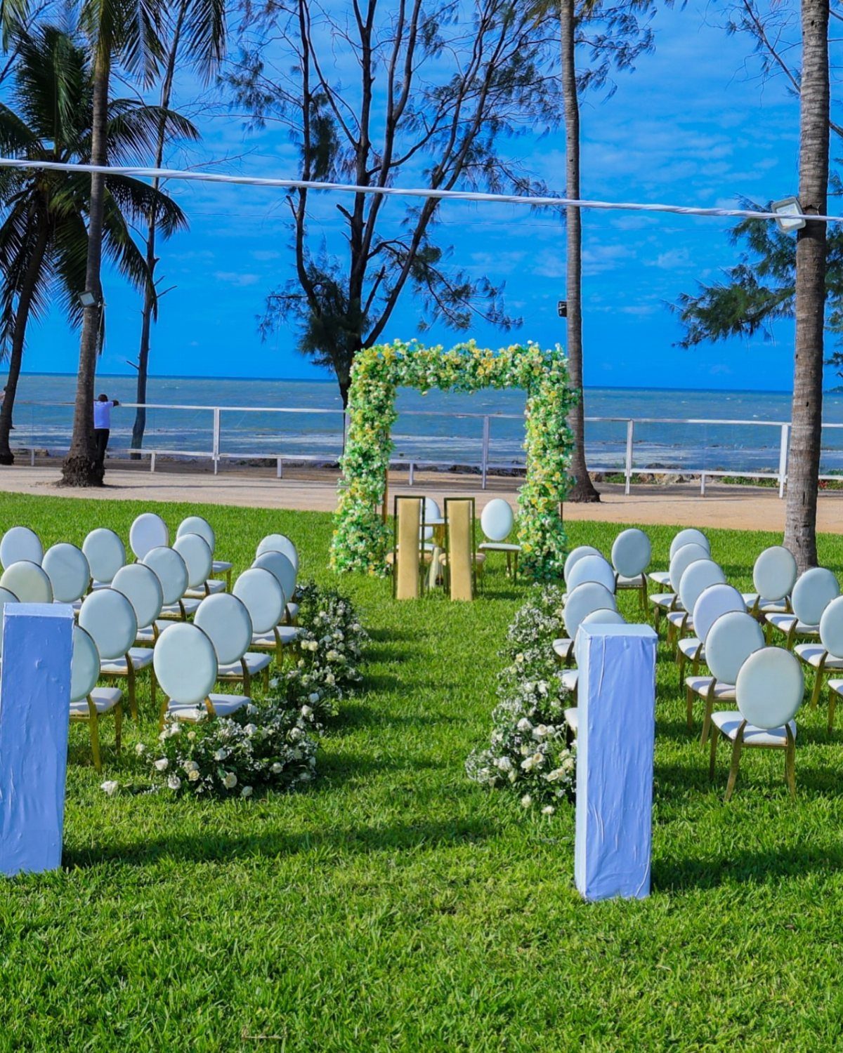 Outdoor wedding ceremony setup with white chairs and floral arch by the ocean