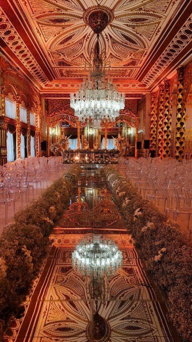 Opulent ballroom with a mirrored table, white flowers, and a grand crystal chandelier.