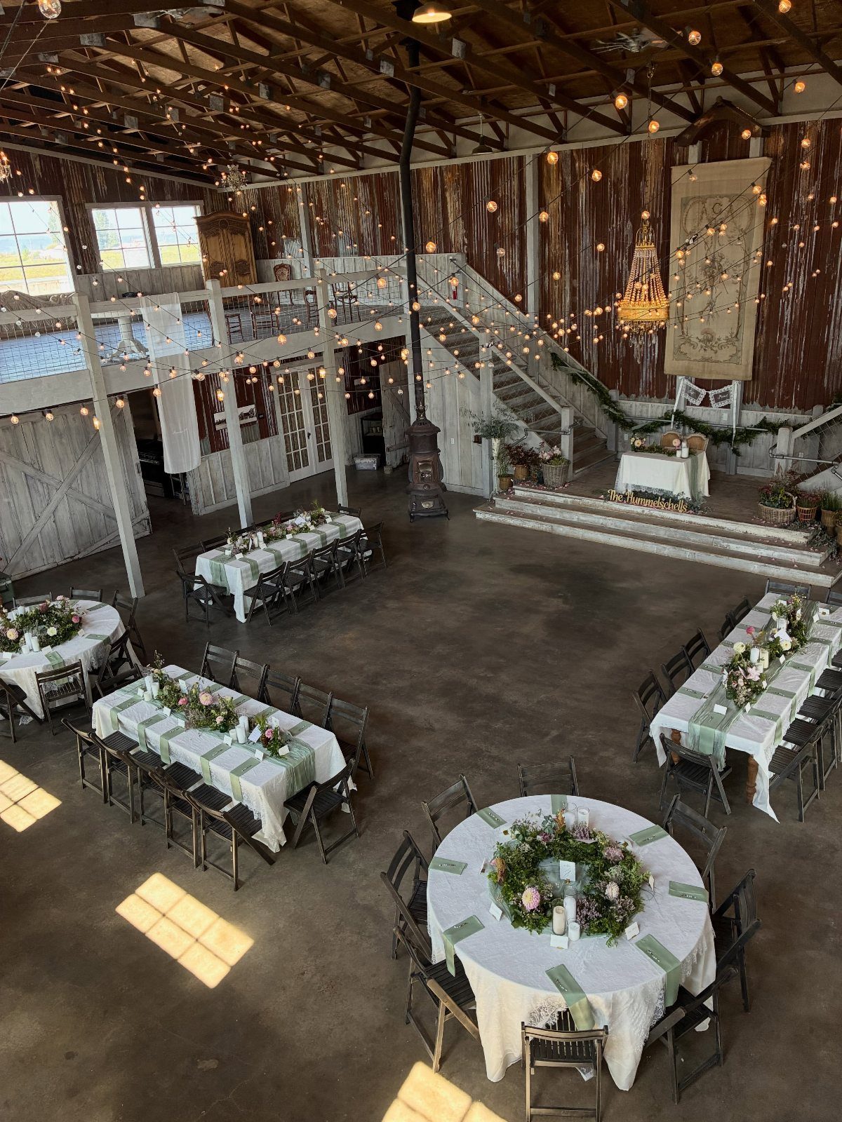 Rustic barn wedding reception with white tables, floral centerpieces, and hanging string lights.