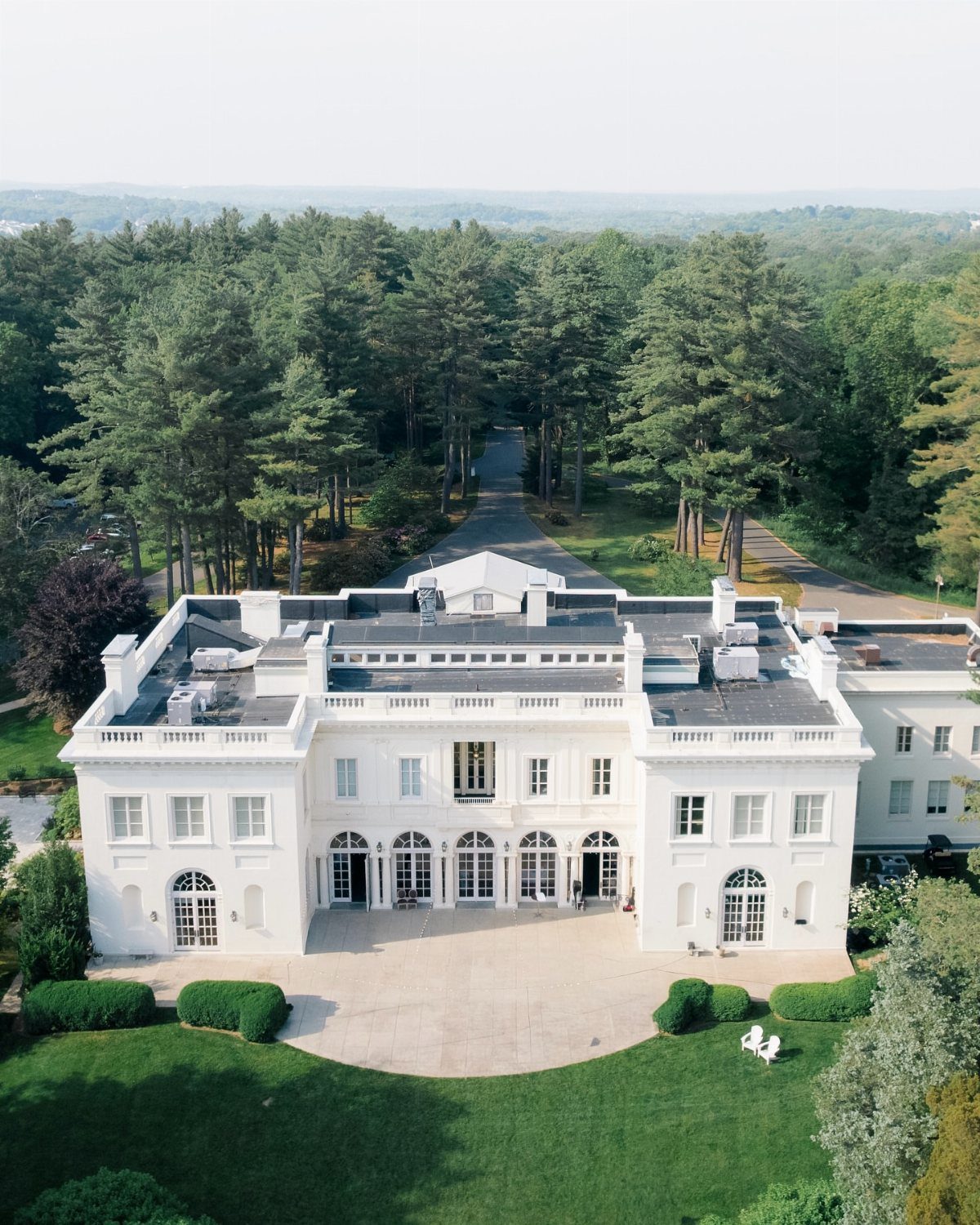 White historic mansion surrounded by green lawns and a dense evergreen forest.