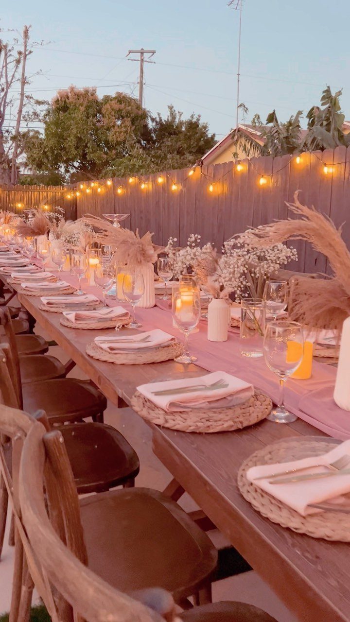 Long wooden dining table with pink runner and string lights in a backyard