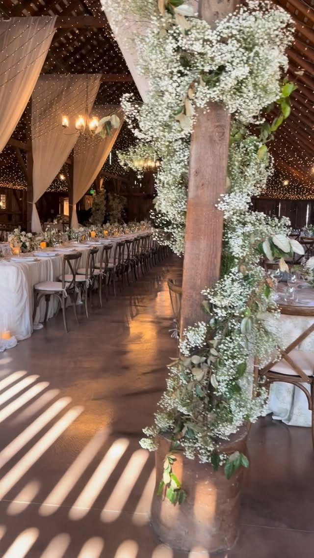 Rustic barn reception venue with long white tables and flower-covered wooden pillars.