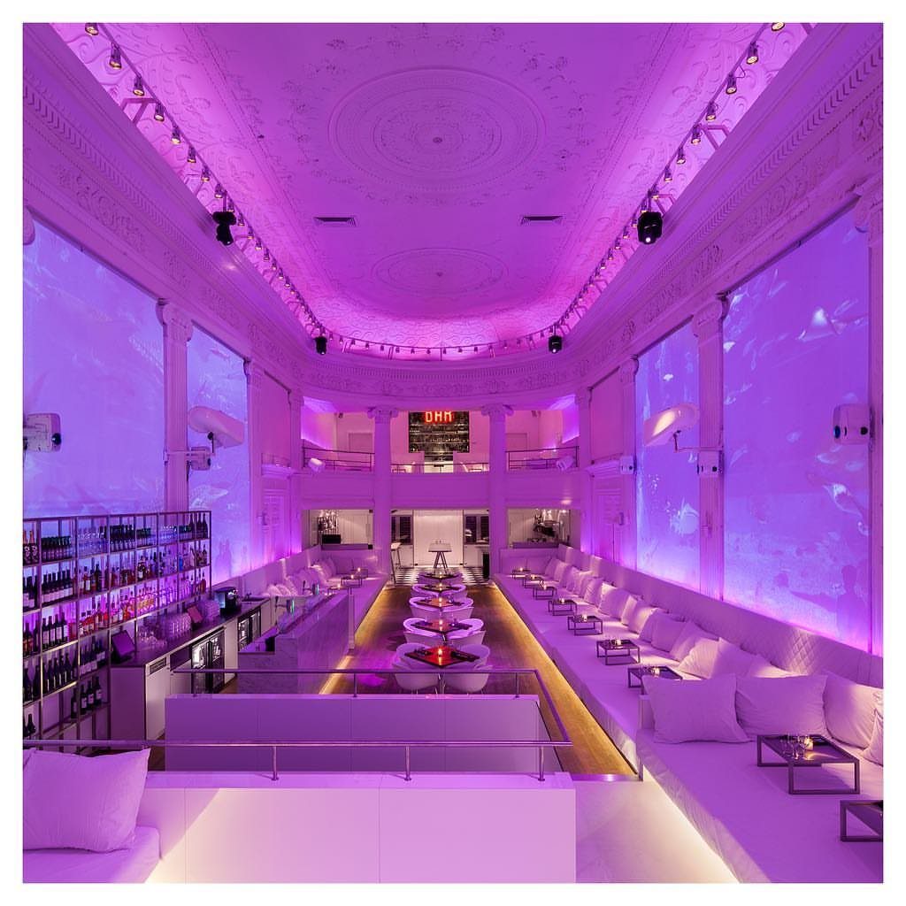 Modern lounge interior with purple lighting, white sofas, and a sleek bar area.
