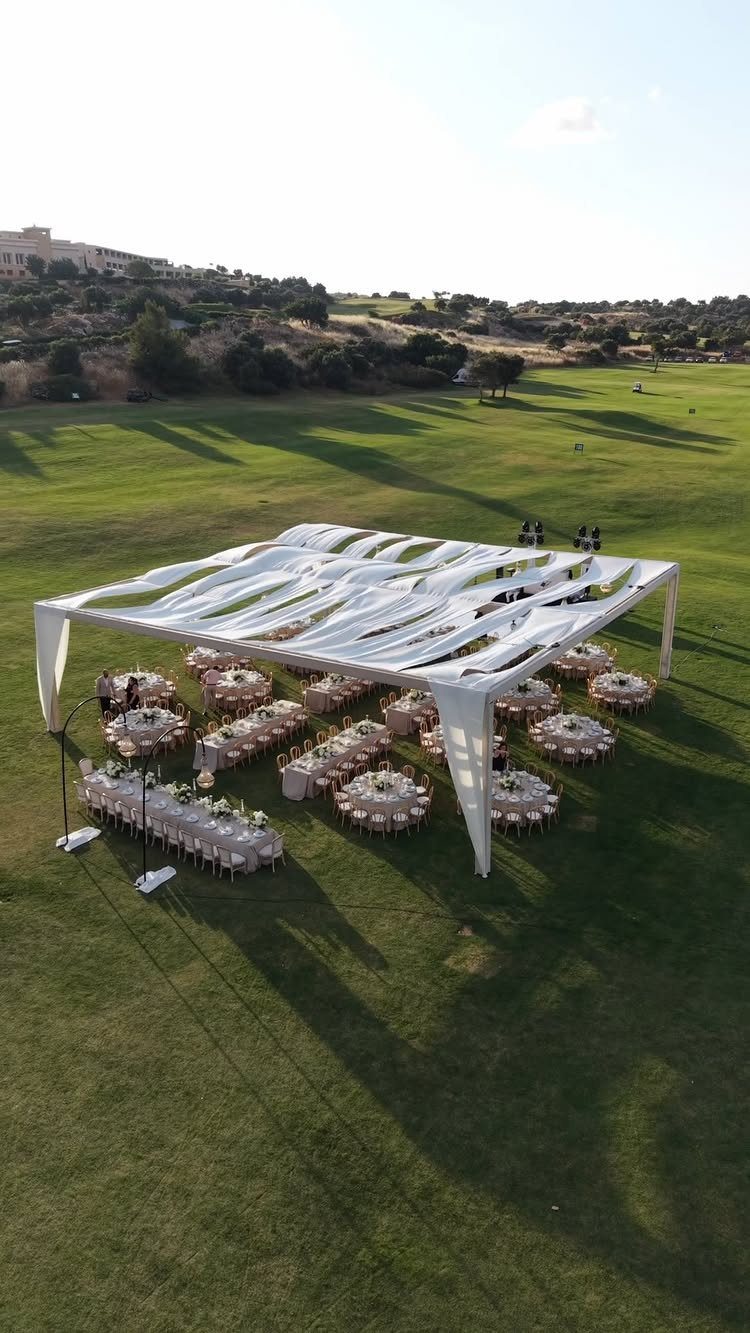 White draped canopy over dining tables on a wide green lawn for reception.