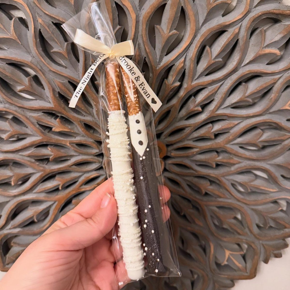 Chocolate covered pretzel rods decorated as a bride and groom in a gift bag