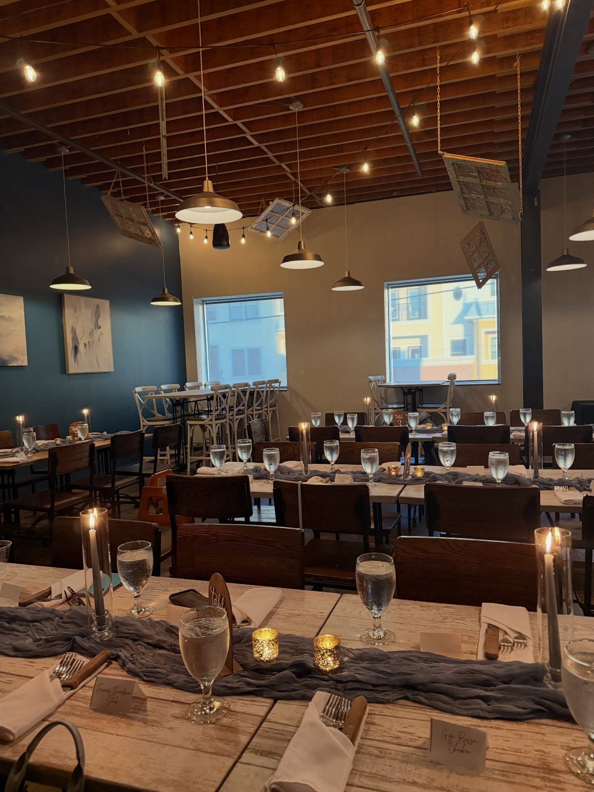 Wooden restaurant tables set with grey runners and candles for a formal dinner.