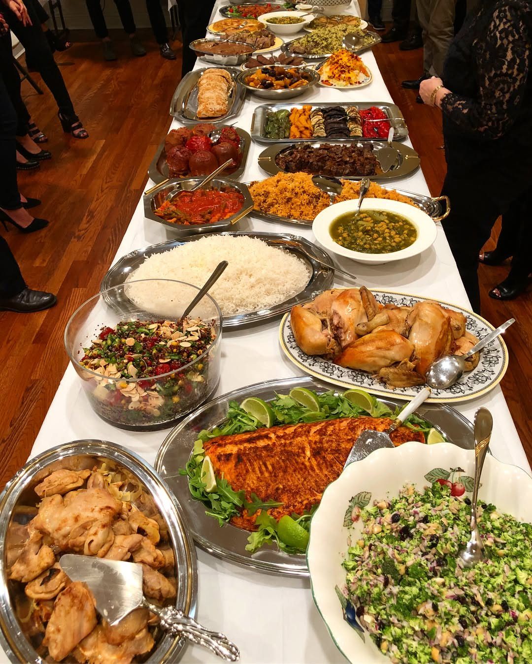 Long buffet table featuring diverse platters of roasted meats, rice, and fresh salads.