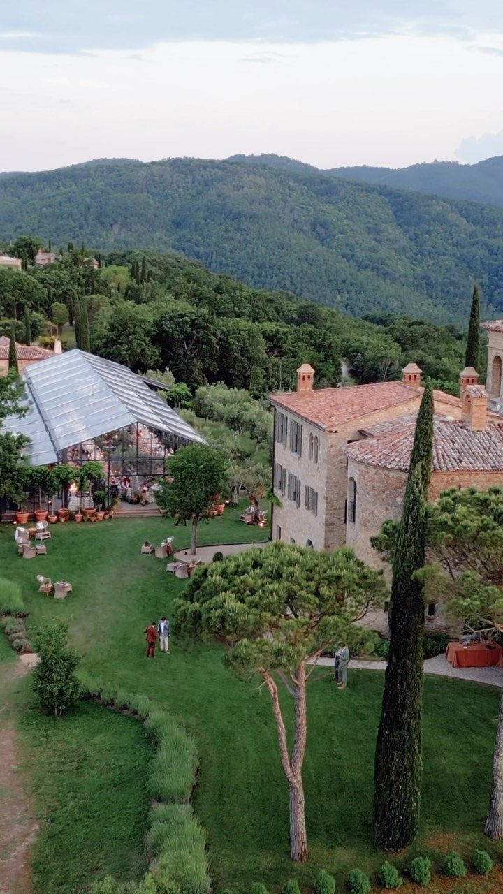 Rustic stone villa and glass greenhouse on a green lawn with mountain backdrop