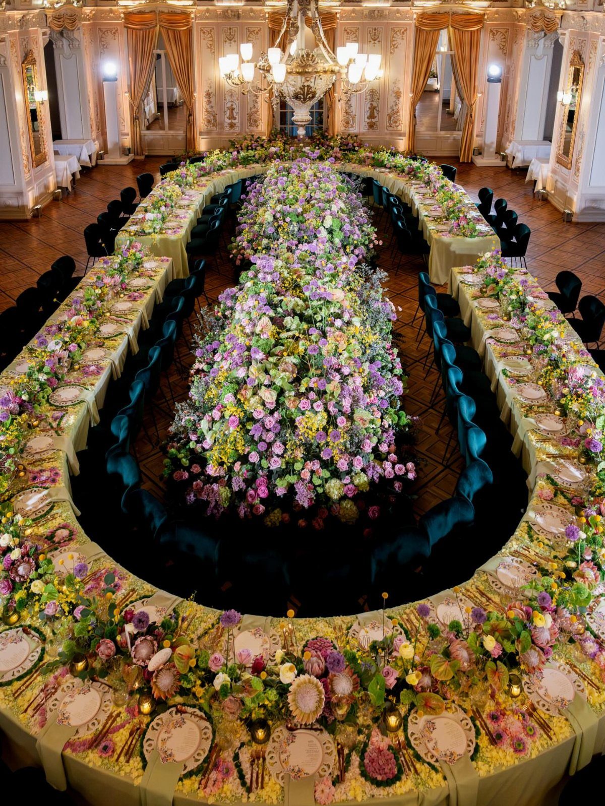 Oval dining table with massive floral centerpieces in a luxurious gold ballroom