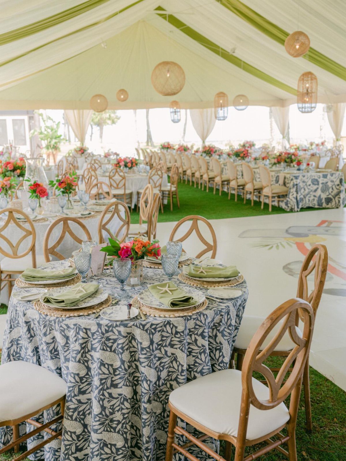 Elegant outdoor event setup under a tent with patterned linens and floral centerpieces.