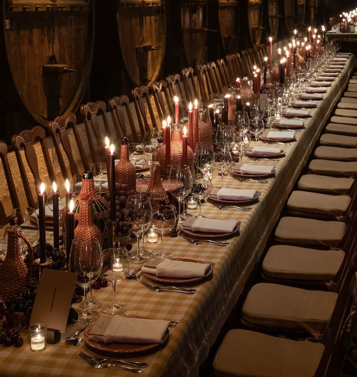 Long banquet table with candles and wine glasses inside a wooden wine cellar