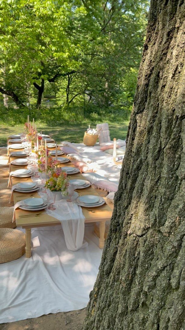 Low wooden dining table with pink flowers and white plates on a garden lawn