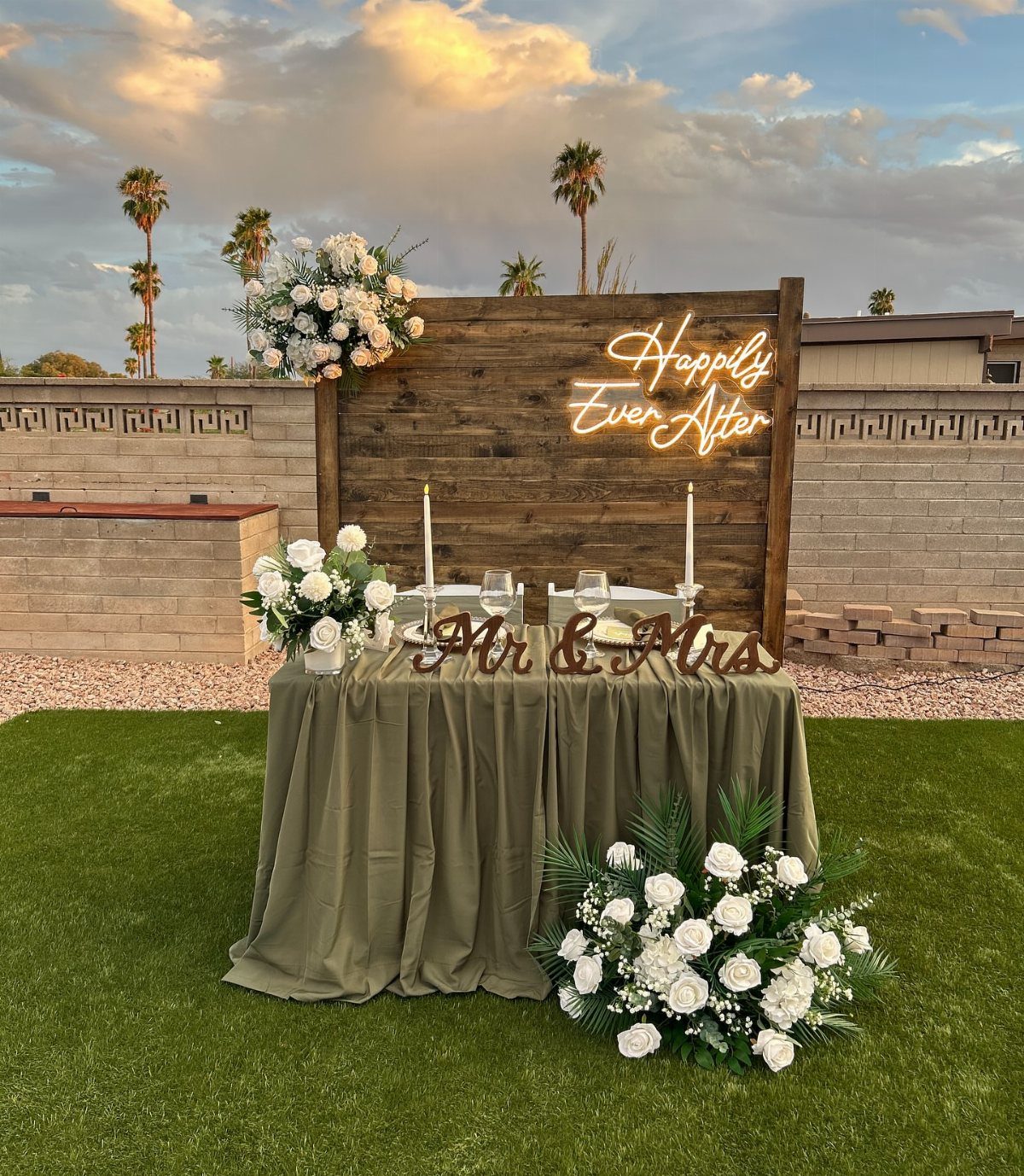 Wedding sweetheart table with olive green cloth and neon sign in a backyard
