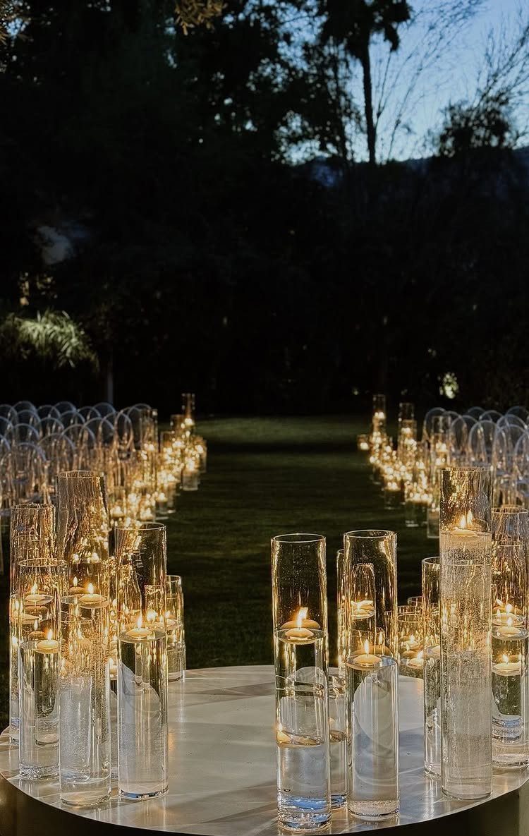 Floating candles in glass cylinders lining a grassy path at dusk for a wedding.