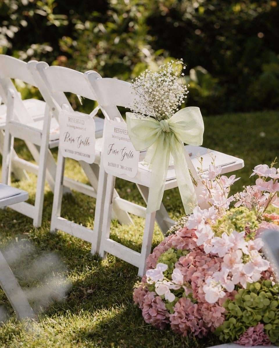 White folding chairs decorated with flowers and bows on a grassy lawn.