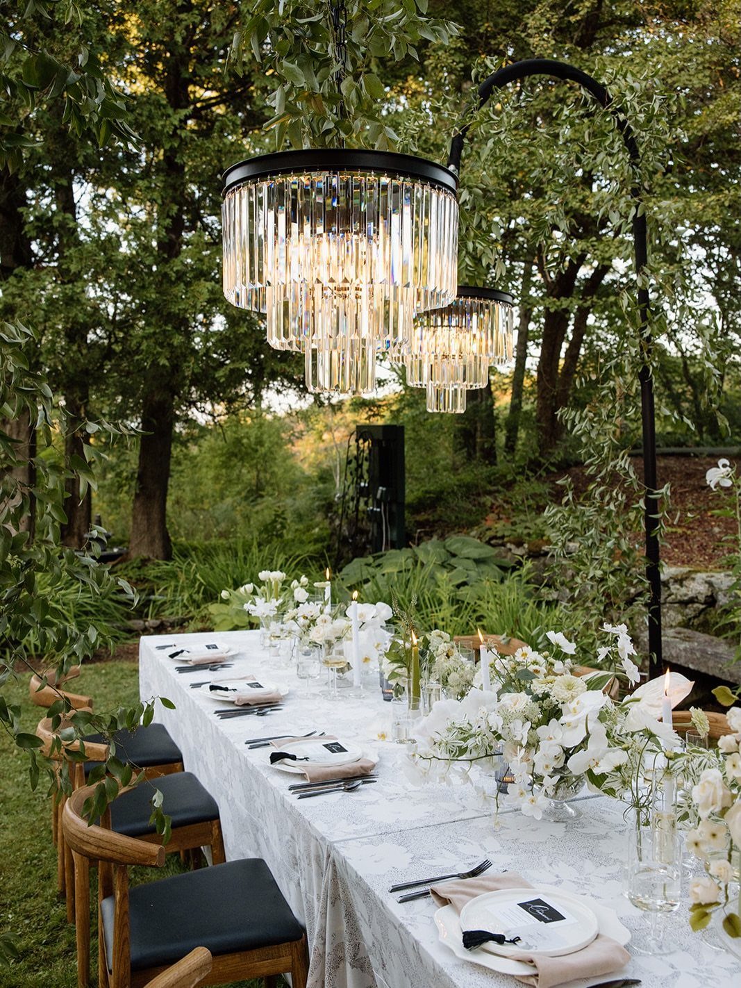 Elegant outdoor wedding table with white flowers and crystal chandeliers in a garden