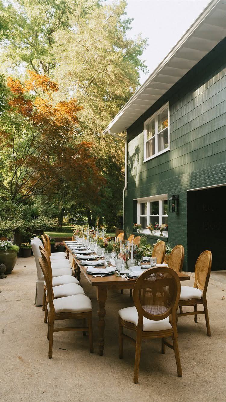 Long wooden dining table with floral centerpieces set on a patio by a house