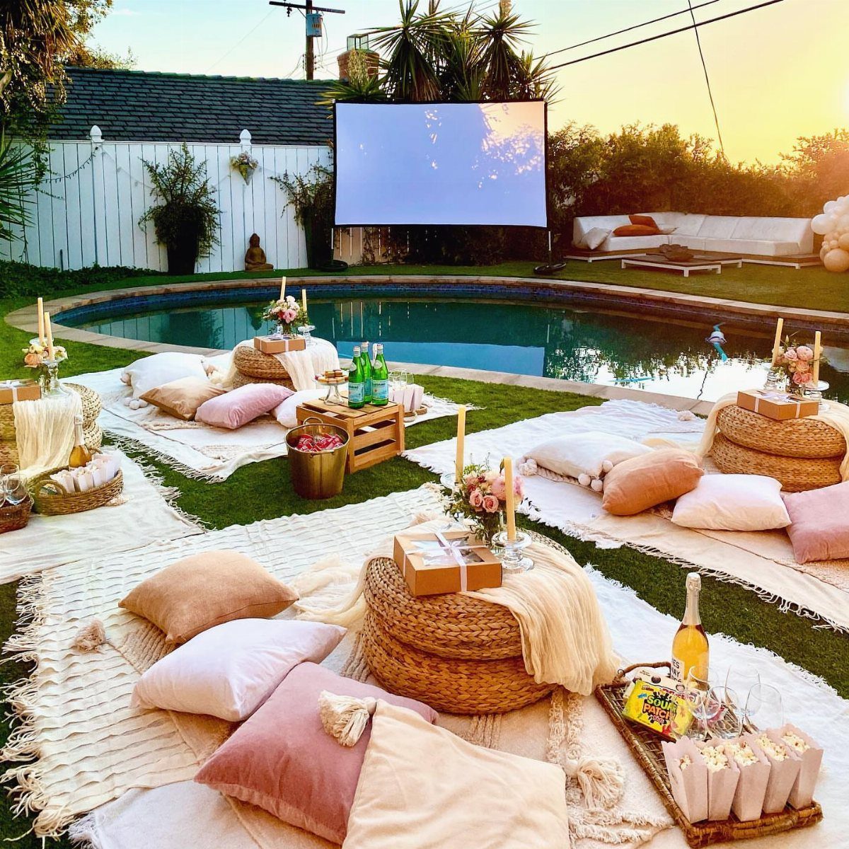 Outdoor movie screen and cozy picnic seating with pillows by a swimming pool