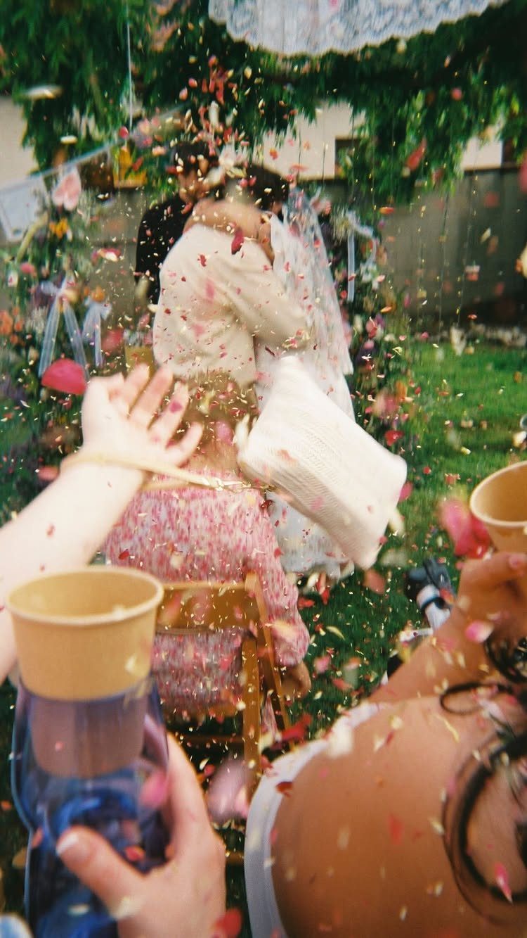 Bride and groom embracing while guests throw colorful flower petals in a garden