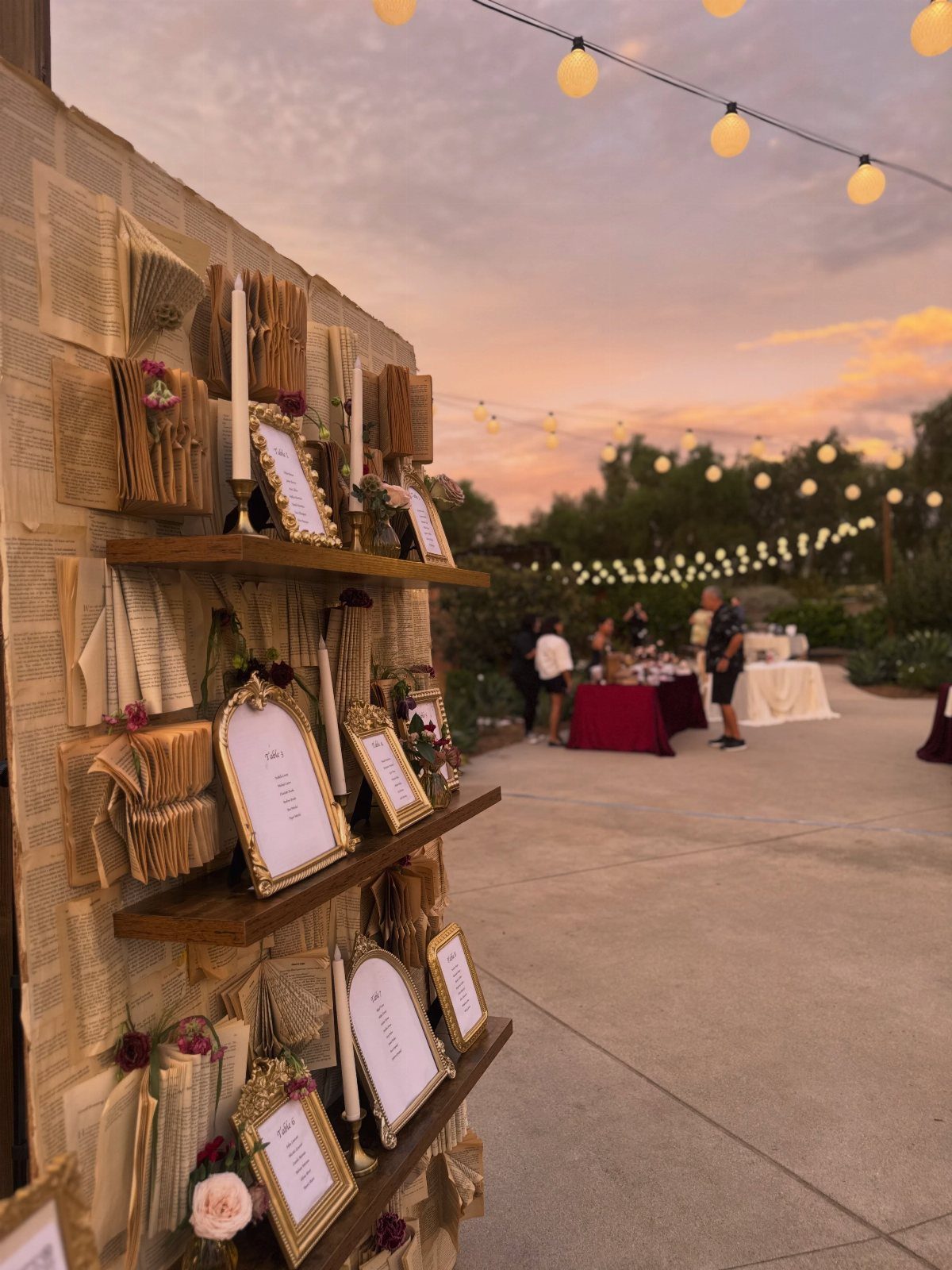 Rustic wedding seating chart with gold frames and candles under outdoor string lights.