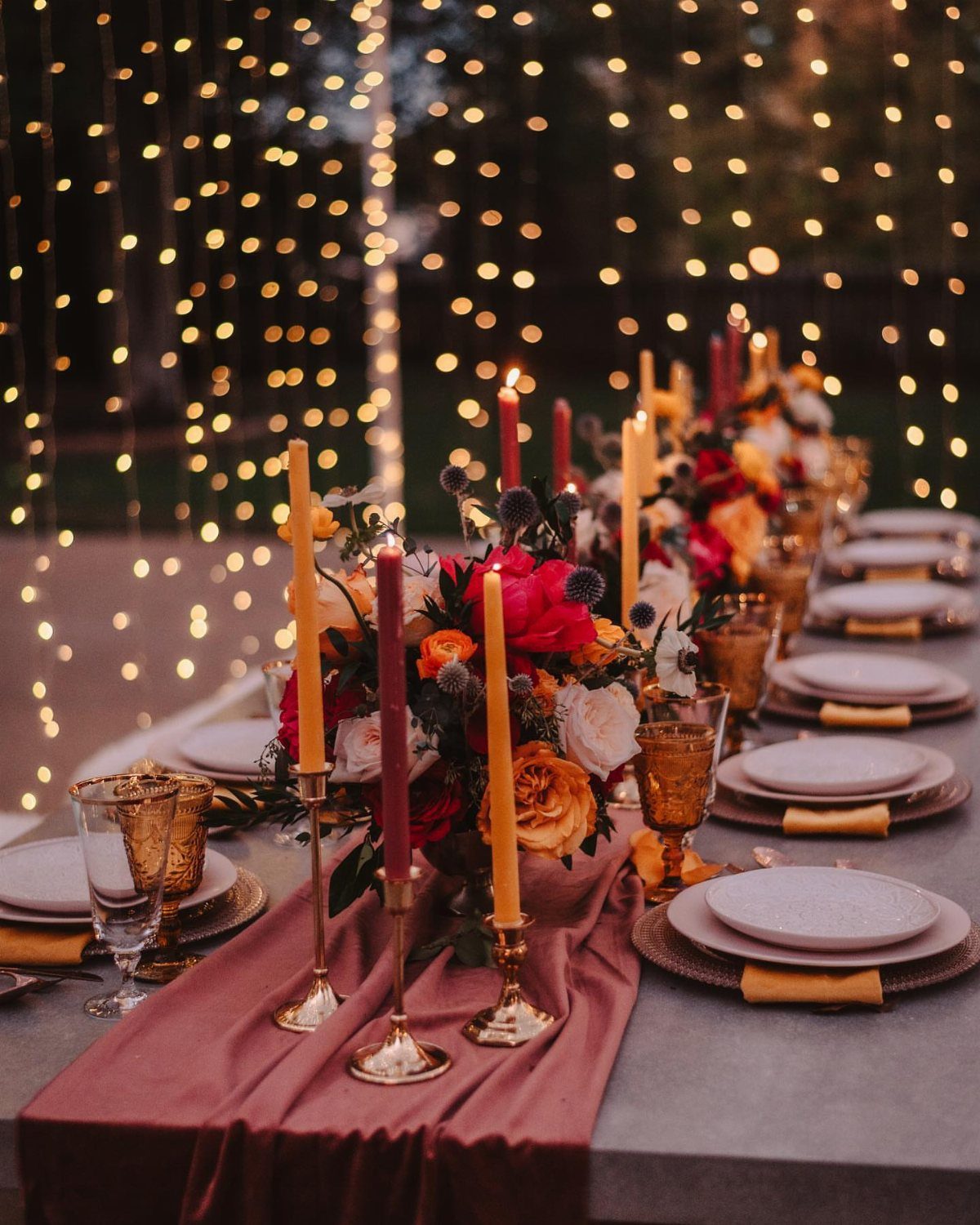 Floral centerpiece with red and orange flowers and tall candles on a wedding table