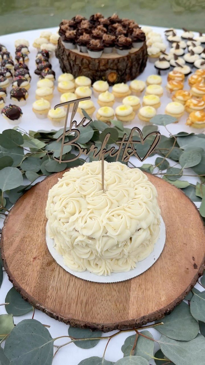 White frosted wedding cake on a rustic wood slice platter with mini desserts.