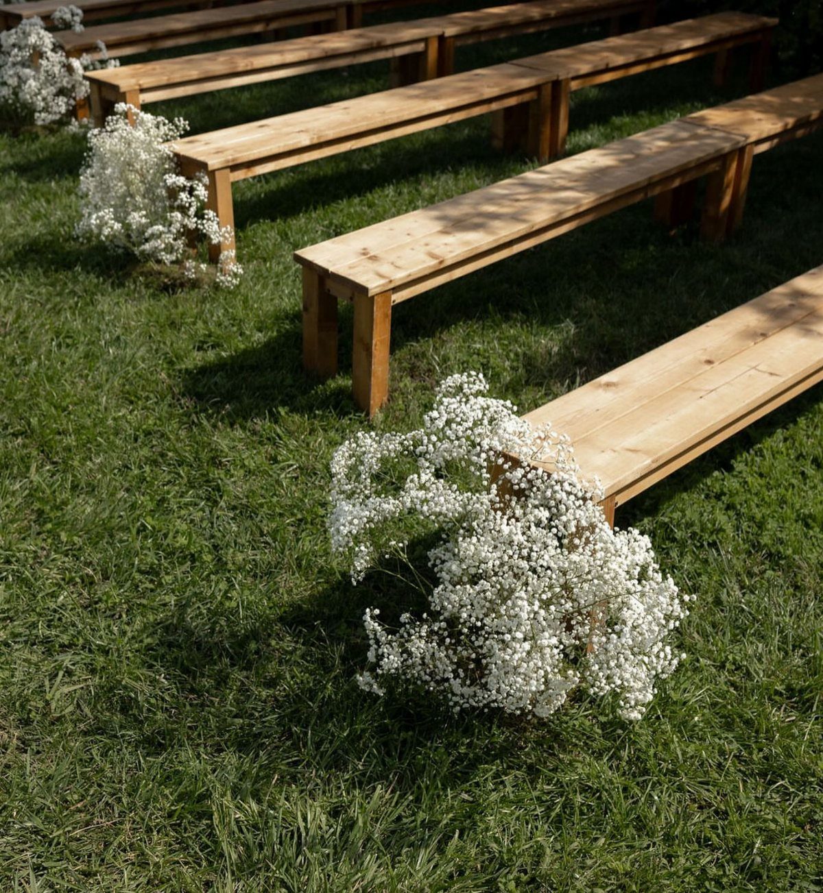 Wooden benches with white baby's breath flowers arranged on a green grass lawn.