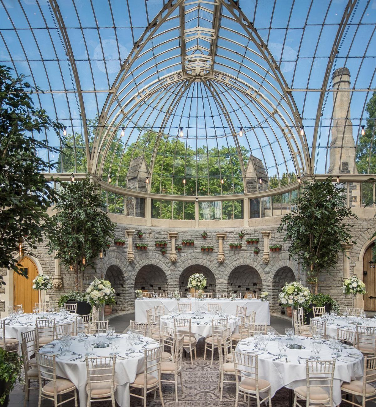 Grand glass conservatory venue set up with white tables and floral centerpieces