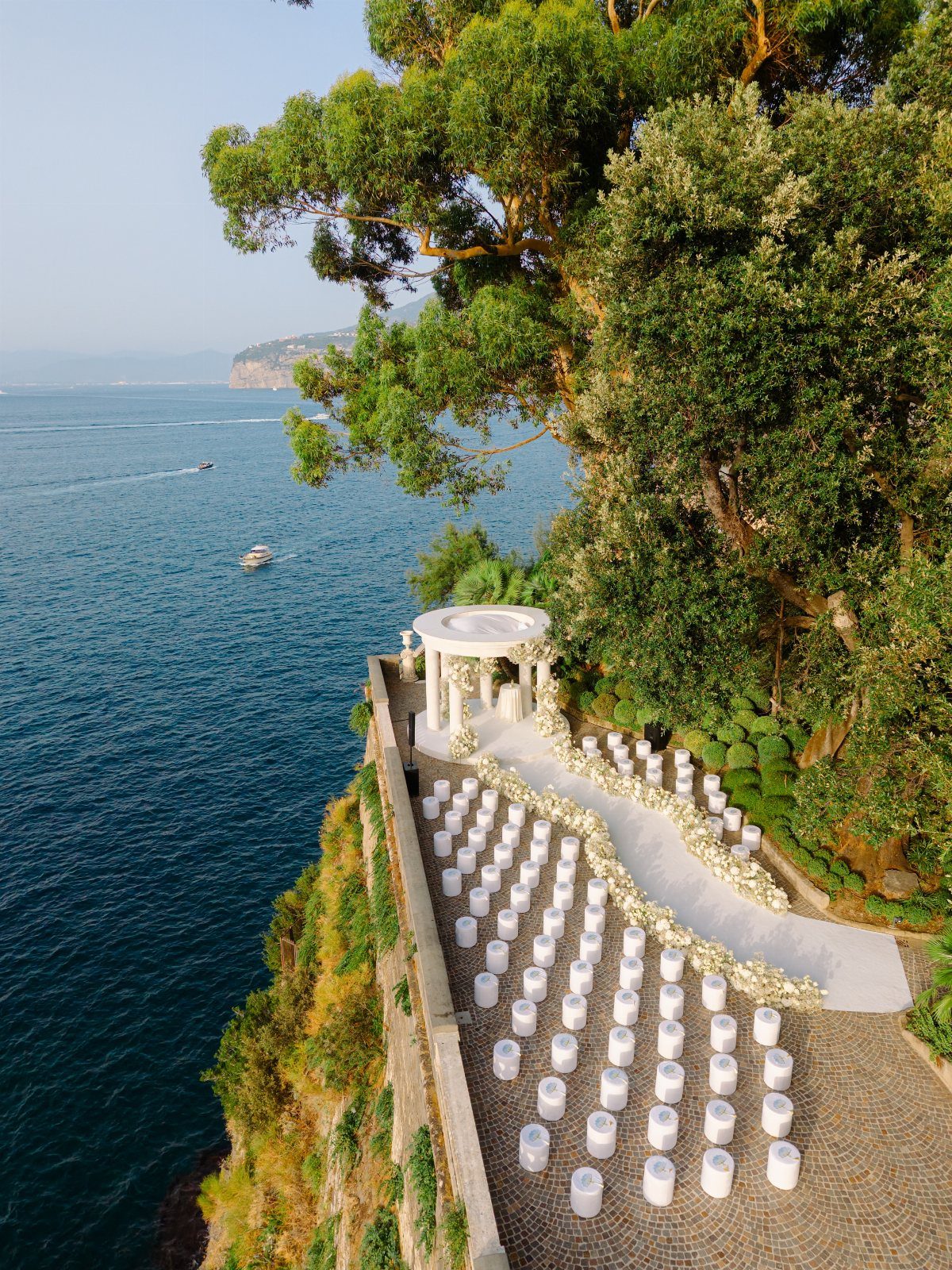 White wedding chairs and a gazebo on a cliff overlooking the blue ocean.