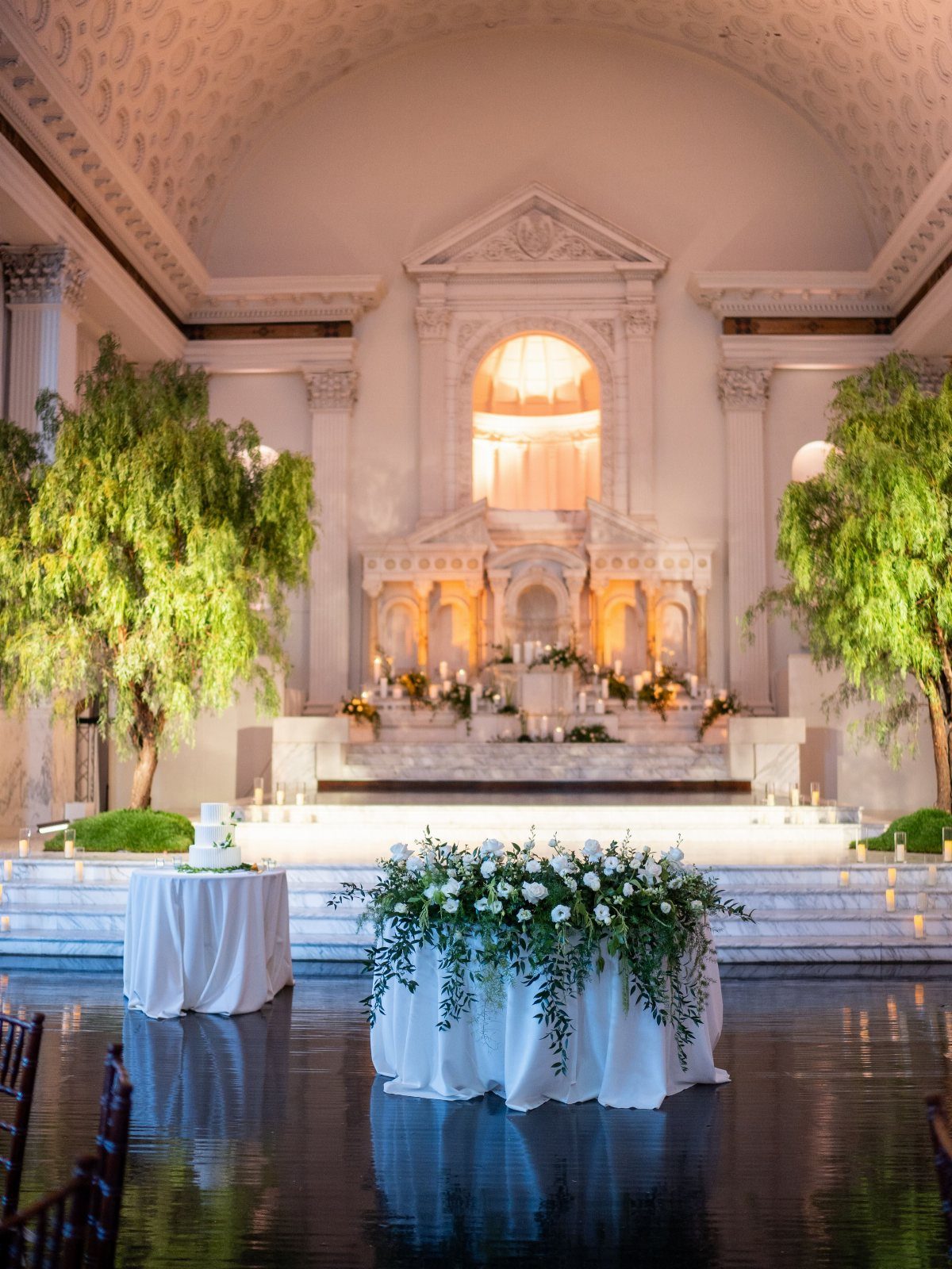 Grand cathedral hall with white columns, floral tables, and large indoor trees.