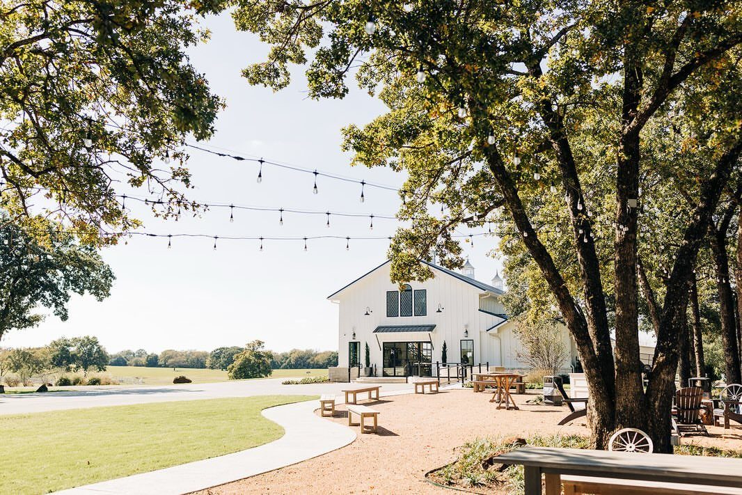 White barn event venue with string lights and large trees in a rural setting