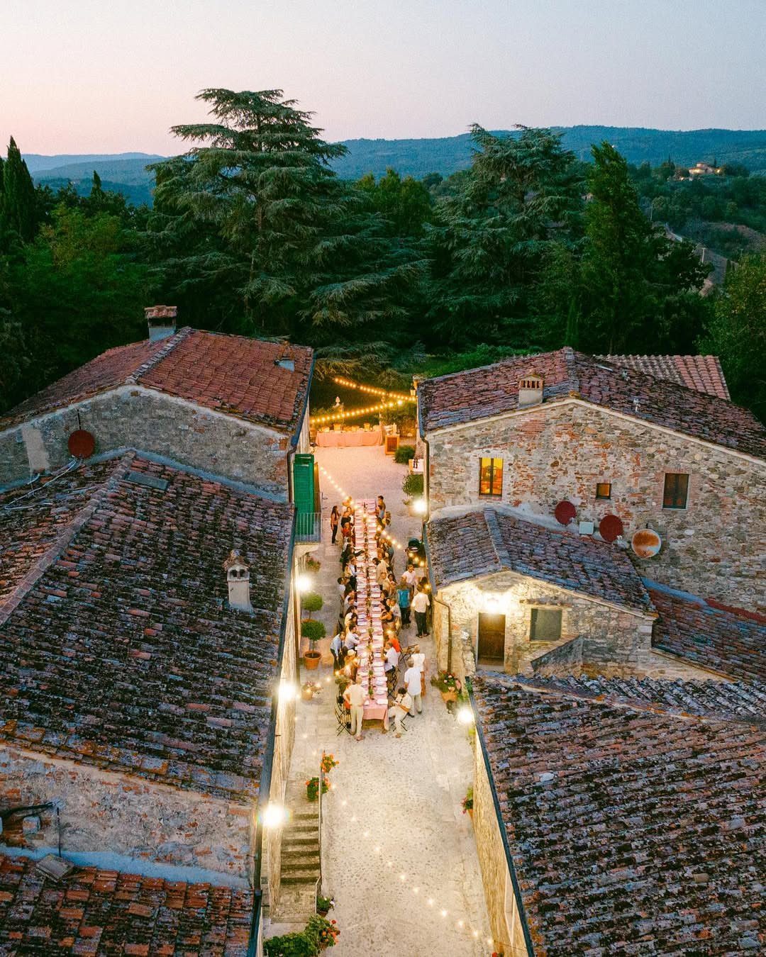Long wedding dinner table set in a rustic stone courtyard with terracotta roofs.