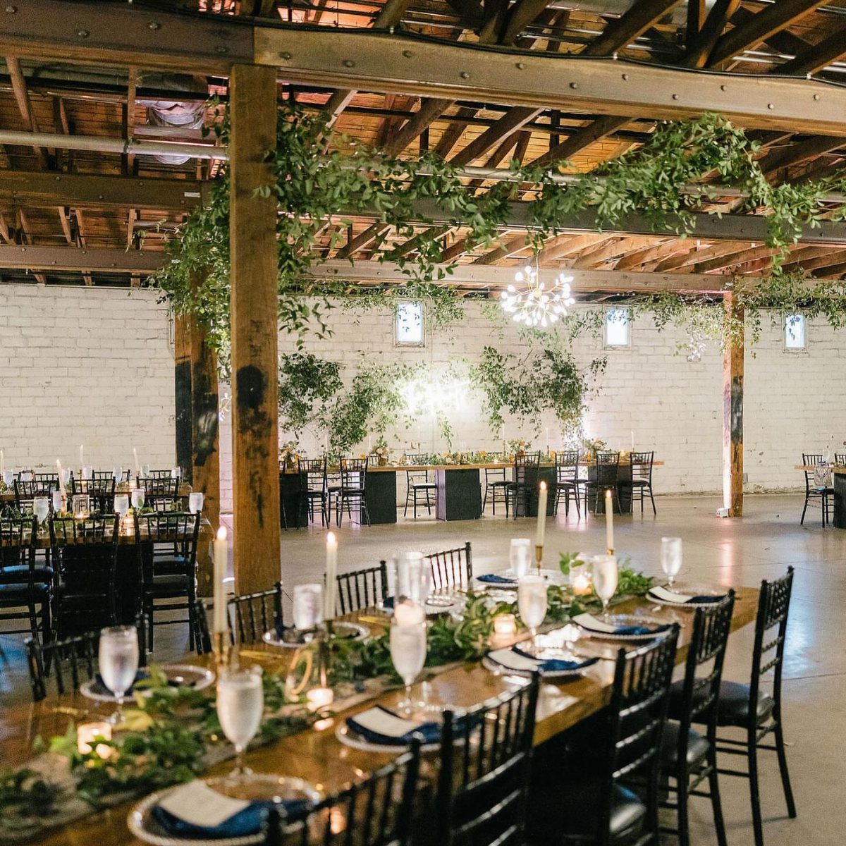 Long wooden dining tables with greenery and blue napkins in an industrial venue.