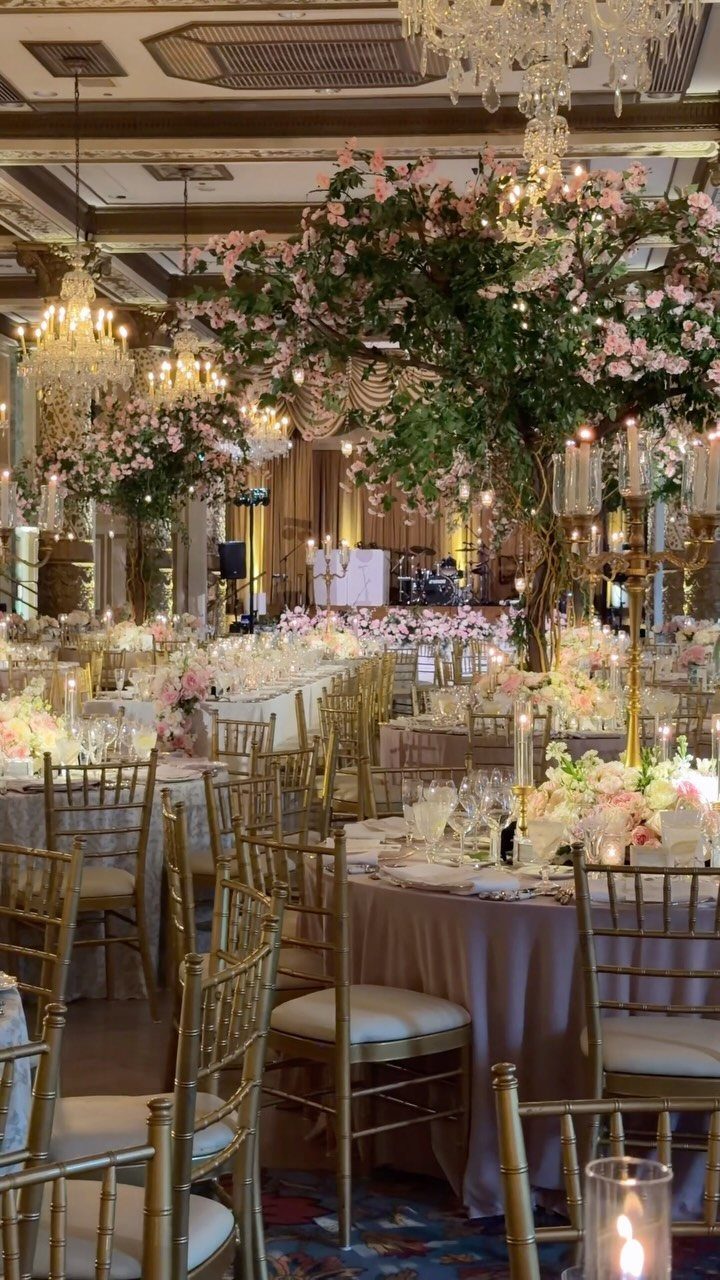 Opulent ballroom with gold chairs, pink floral centerpieces, and crystal chandeliers.